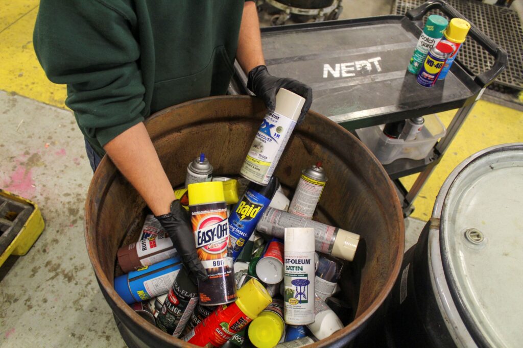 NEDT technician holds up a grill cleaner product above a container of aerosol cans.