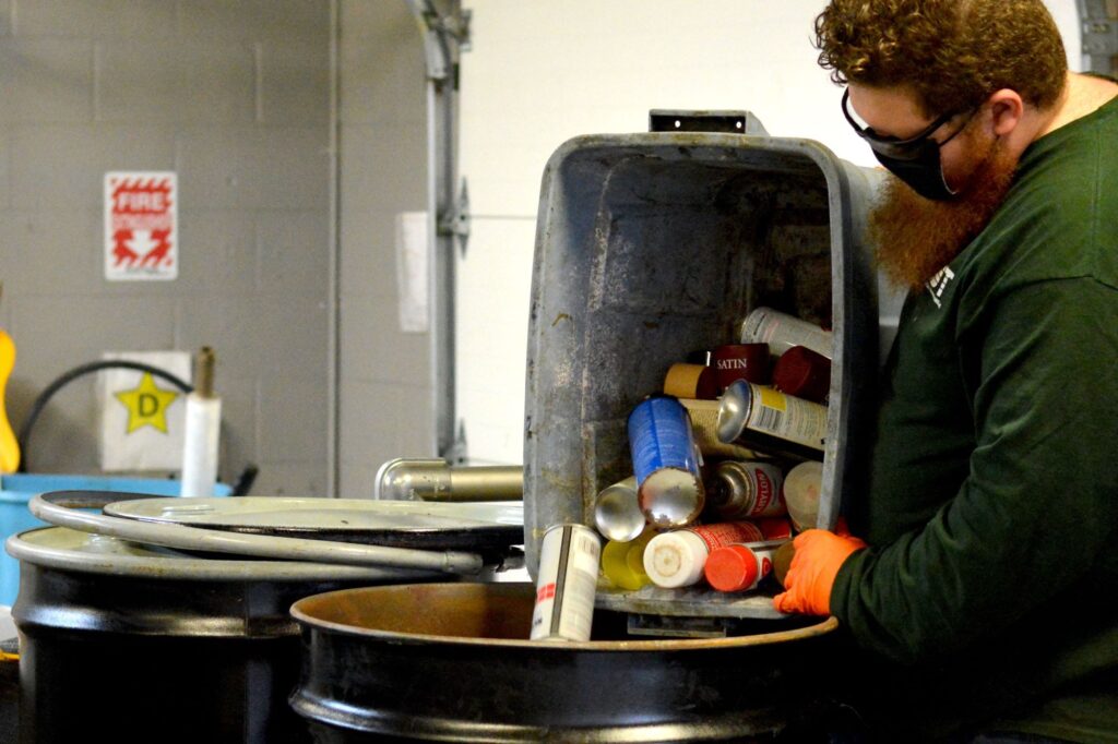 NEDT technician dumping aerosol spray cans into hazardous waste barrel.