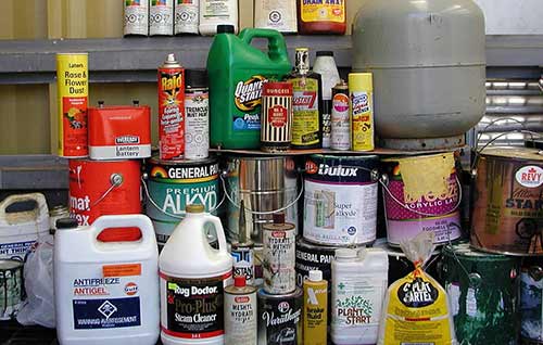 Hazardous waste including pesticides, cleaning products, paints, and stains stacked in a pile.