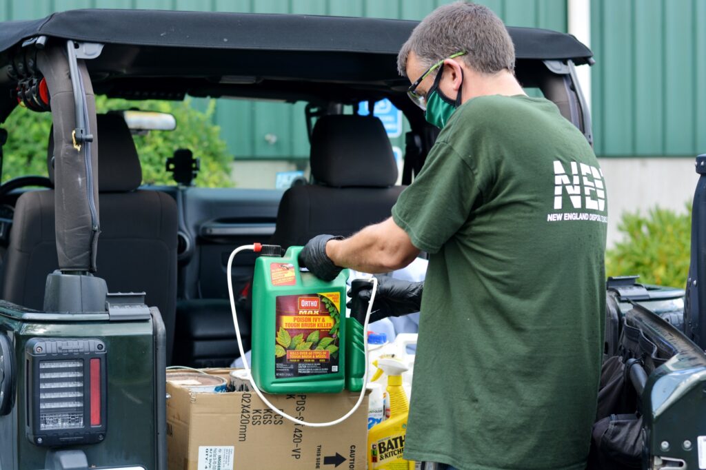 NEDT employee hauling hazardous waste into the back of a truck while wearing gloves and a mask.