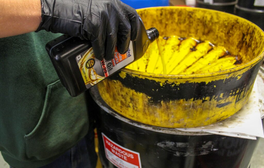 NEDT employee pouring used motor oil into a hazardous waste drum for disposal.