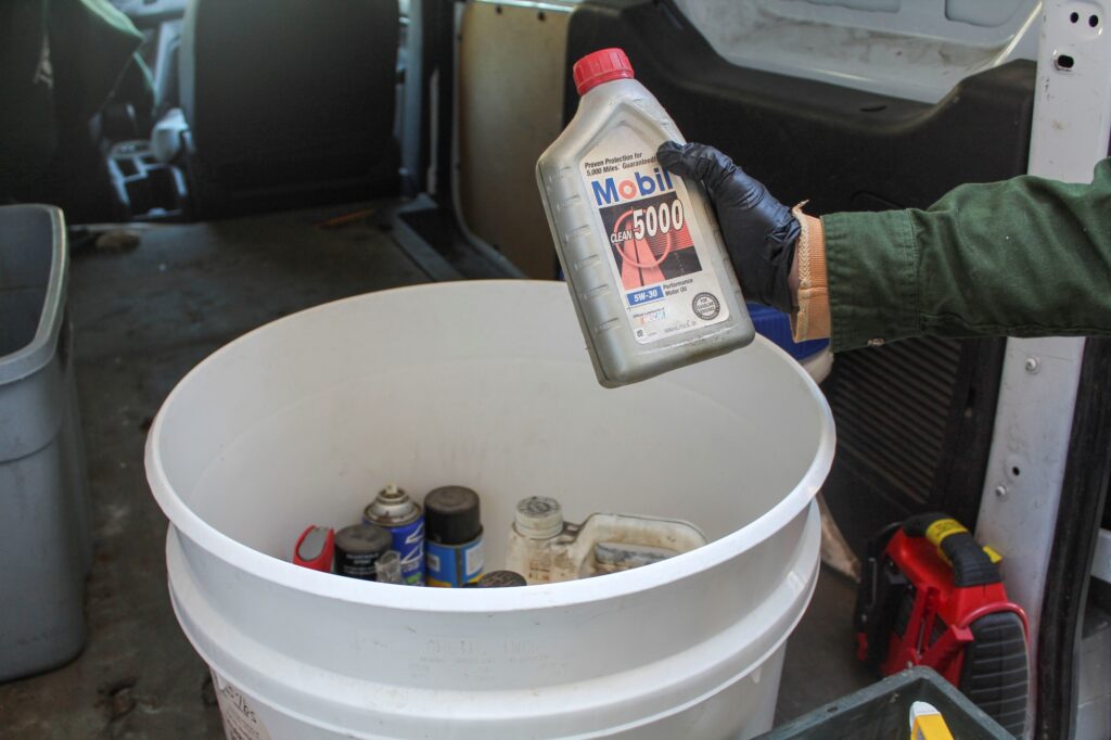 NEDT staffer placing motor oil into a containers alongside other Petroleum-Based Products.