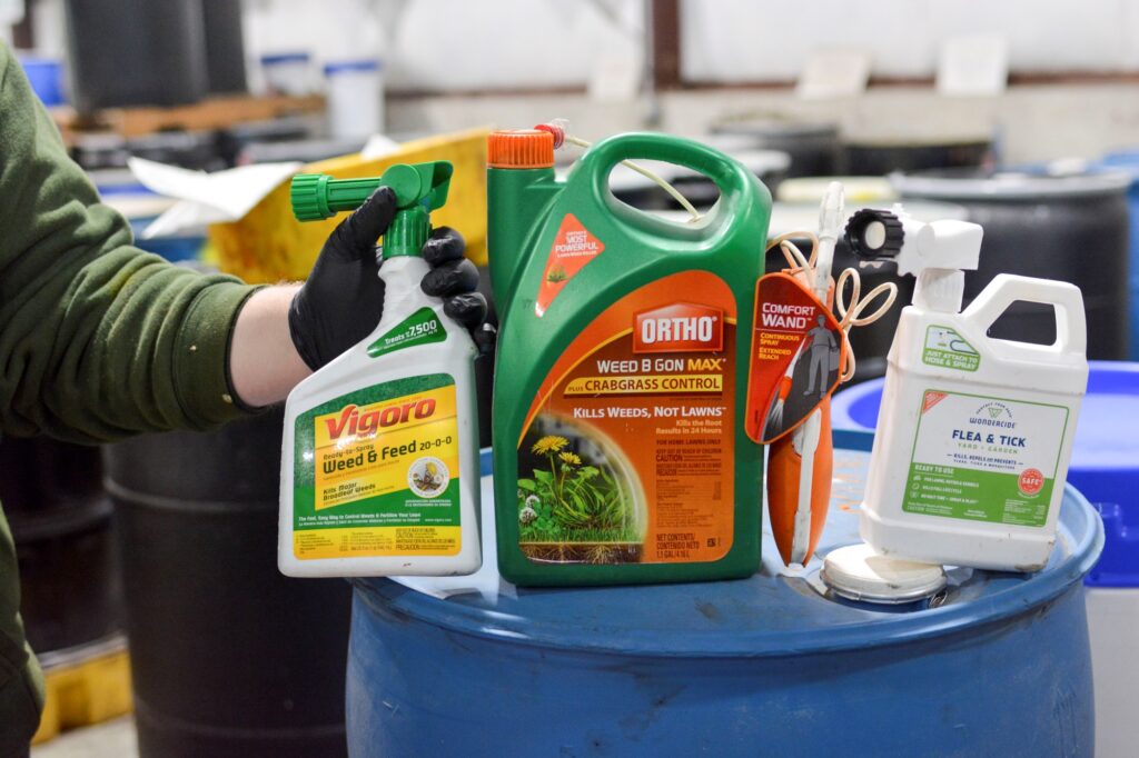 NEDT staff holds bottle of herbicide alongside other household pesticides.